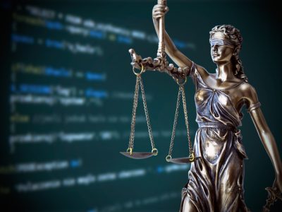 Justice statue with code on screen in background. Internet crime concept